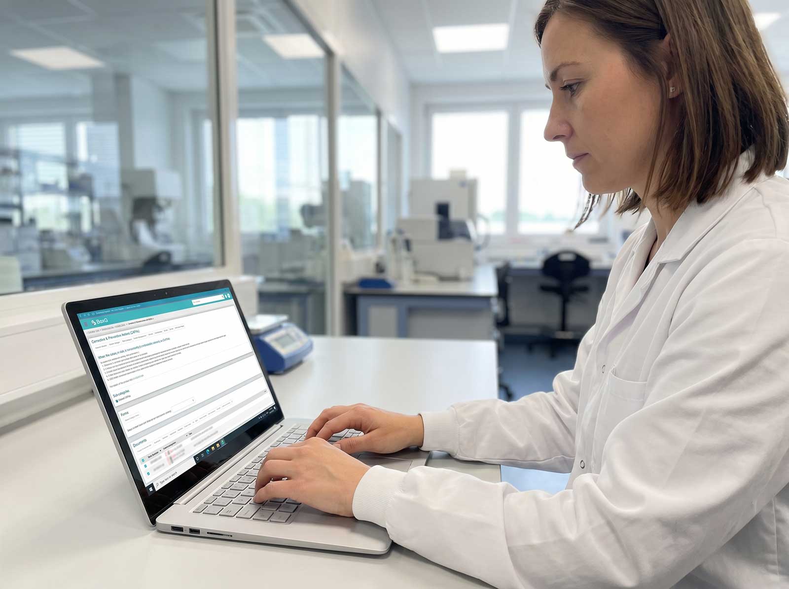 Image 3 (woman, MacBook, open-plan office):
Professional woman using BaxQ document control and review software on a laptop in a modern open-plan office, BaxMed regulatory compliance platform