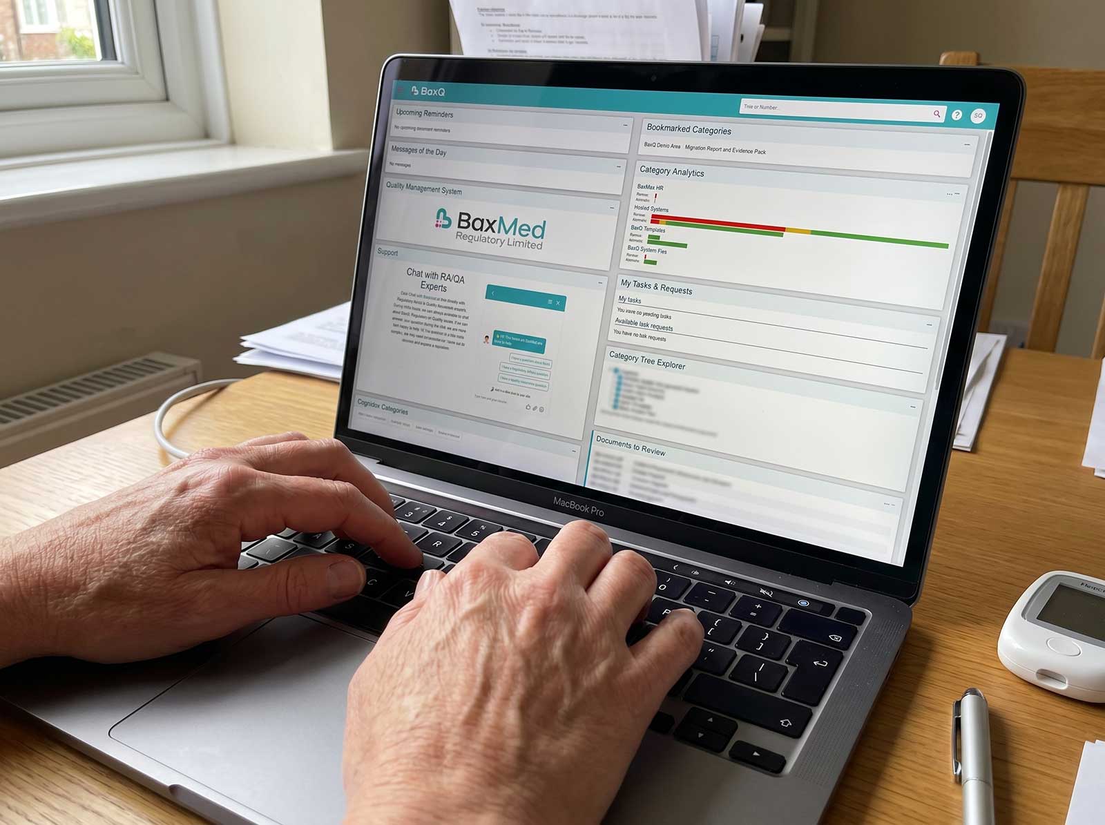 Close-up of hands typing on a MacBook Pro displaying the BaxQ quality management system dashboard with BaxMed Regulatory Limited branding, medical device compliance software