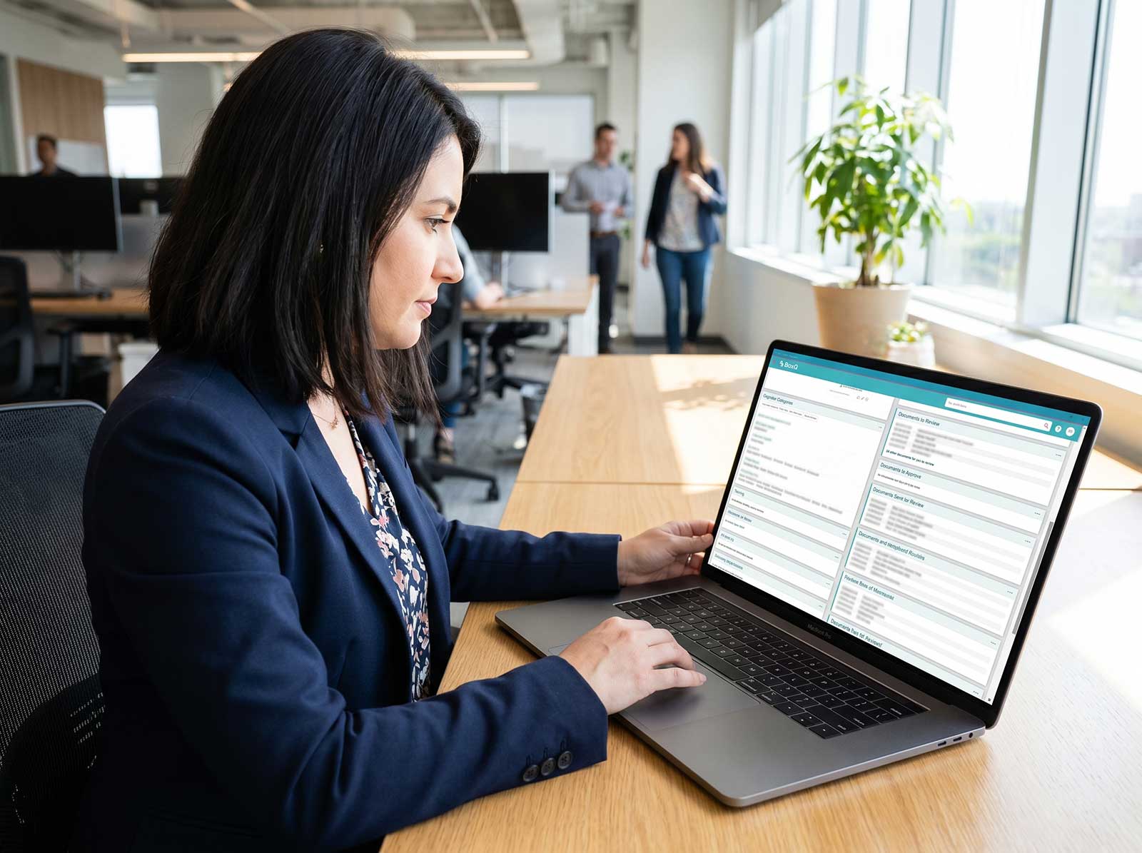 Professional woman using BaxQ document control and review software on a laptop in a modern open-plan office, BaxMed regulatory compliance platform